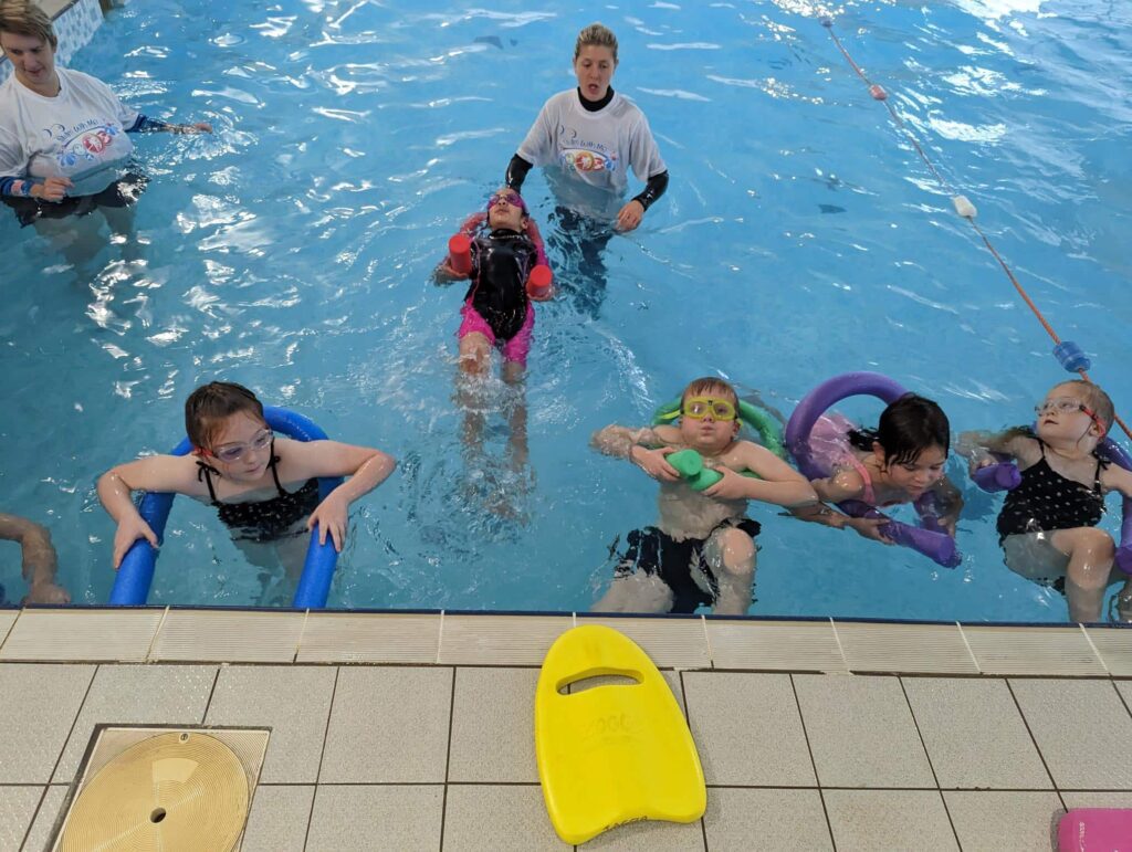 Swimming instructors teach water confidence to a group of children in a pool