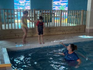 Two children aged 8 & 4 standing on edge of pool enjoy the benefits of swimming lessons from Tracie at Swim-With-Me