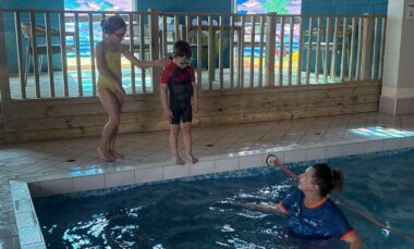 Two children aged 8 & 4 standing on edge of pool enjoy the benefits of swimming lessons from Tracie at Swim-With-Me